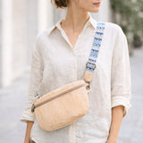 Person wearing a beige crossbody bag with a blue strap in an outdoor setting